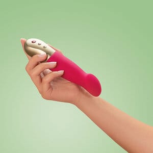 Fun Factory Sundaze pulsaattori punaisena, kullanvärisellä ohjauspaneelilla, kädessä pideltävänä vihreää taustaa vasten