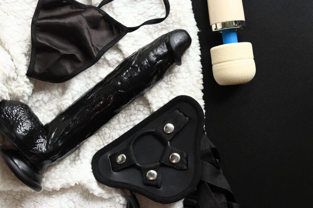 Musta jättidildo, harness-valjaat ja wand-vibraattori makuualustalla – XL dildojen suositusartikkelin kansikuva